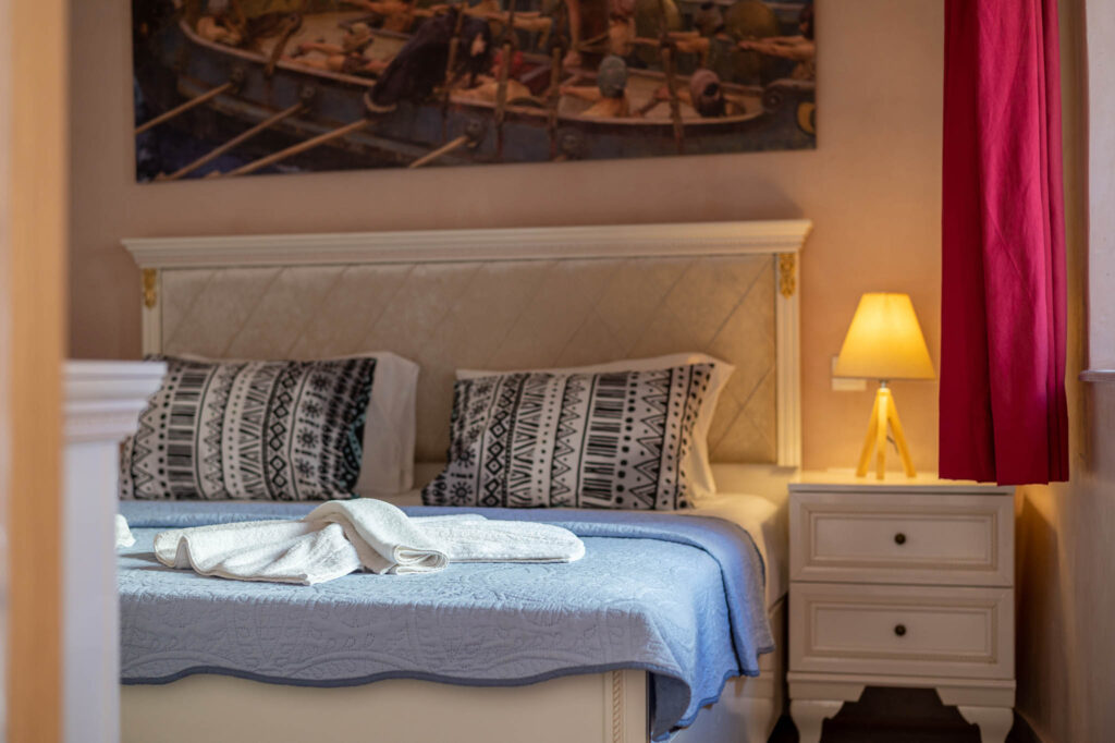 A white color king size bed with blue/white bed linen, a picture on the wall, red curtains in Aspasias house in Zakros/Crete