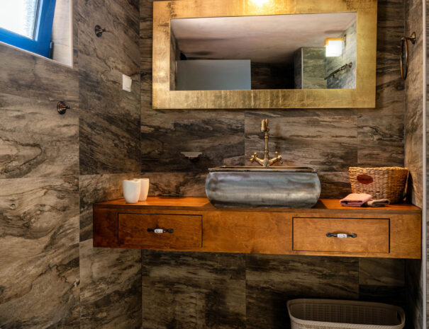 Vintage bathroom with golden and wooden colors, a blue window and a white toilet in a holiday home in Zakros