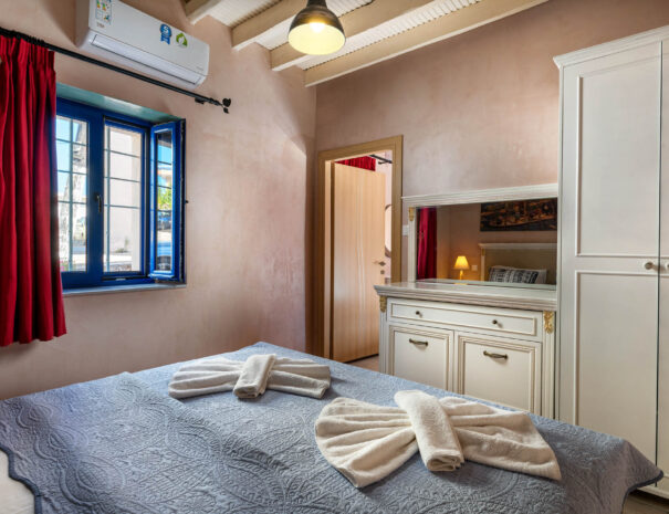 Sleeping room in a holiday home with a kingsize bed, a white wardrobe, a white dresser and a red curtain in front of the blue window