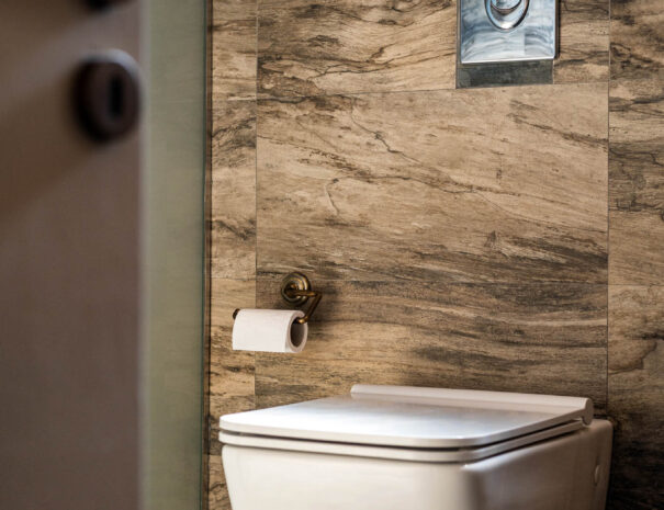 A whitetoilet seat with flusher and toilet paper in a brown bathroom